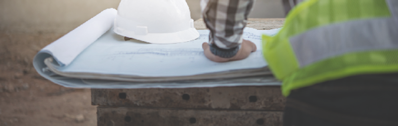 Construction worker looking at drawings laid on concrete slabs